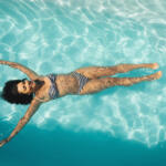 High angle view of young mixed-race woman floating in swimming pool in backyard of her home