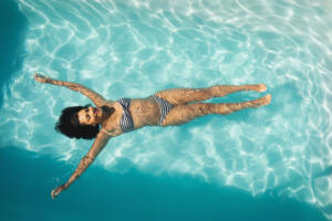 High angle view of young mixed-race woman floating in swimming pool in backyard of her home