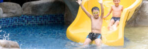 Young Asian Thai boy play water slider in a park during summer time.