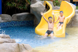 Young Asian Thai boy play water slider in a park during summer time.